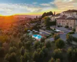 Un tramonto dorato illumina un agriturismo con piscina, immerso tra ulivi e colline, perfetto per un tour della Toscana.