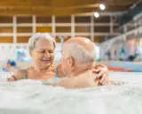 Uśmiechnięta para seniorów relaksuje się w jacuzzi w basenie. To wspaniałe miejsce, jak sanatorium szpitalne, gdzie można odzyskać siły.