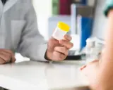 Lekarz podaje pacjentowi pojemnik na mocz, sugerując potrzebę diagnostyki w kierunku krwiomoczu, co jest pierwszym krokiem do ustalenia leczenia domowego.