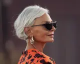 Elegante Frau mit Kurzhaarfrisur ab 60, Sonnenbrille und auffälligem Ohrring.