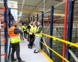 Grupa osób w kamizelkach odblaskowych zwiedza magazyn CEVA Logistics. To potencjalna ceva logistics praca.