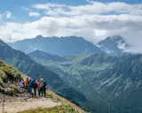 Grupa turystów odpoczywa na szlaku z widokiem na majestatyczne Tatry. W oddali majaczy Kasprowy Wierch, otoczony chmurami.