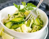 Frischer Zucchini-Salat mit Petersilie und Limettenspalten, serviert in einer weißen Schüssel. Eine Gabel steckt im Salat.