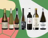 Seis botellas de vino blanco, algunas con etiquetas que sugieren ser vino típico de Bilbao, dispuestas sobre un fondo verde y rosa.
