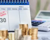 Kalendarz z zaznaczonym "Pay off Debts!" i sterty monet. Długi w ZUS to jak więzienie, ale spłata to wolność.