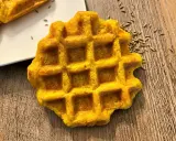Gaufre carotte dorée, parsemée de graines sur fond de bois. Un délice orangé à déguster.
