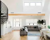 Ampio soggiorno con scala a chiocciola nera, divano angolare grigio e trave in legno a vista. Loft idee originali per un ambiente moderno.