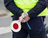 Policjant w kamizelce odblaskowej trzyma za plecami lizak do zatrzymywania pojazdów.