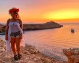Ragazza con foulard rosso e top bianco, shorts di jeans e sandali, con tramonto spettacolare su Ibiza. L'outfit perfetto per come vestirsi a Ibiza.