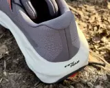 Szary but Salomon Ultra Glide 3 z białą podeszwą i napisem "energy FOAM" na tle leśnej ściółki.