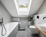 Un piccolo bagno sottotetto basso con vasca, WC, lavabo e lucernario.