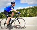 Ciclista in maglia blu affronta la **salita** del **Mont Ventoux**, con la cima innevata in lontananza.