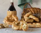 Pane intrecciato e ciambelle, ispirazione per ricette ciociare, accanto a una bottiglia di vino rosso e un cesto di vimini.