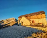 Il rifugio Duca degli Abruzzi, con la sua struttura in pietra e legno, si erge maestoso al tramonto, dominando un paesaggio montano aspro e solitario.