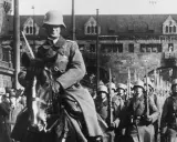 Soldaten marschieren in Formation, ein Reiter führt sie an. Ein historisches Bild der Rheinlandbesetzung 1936.