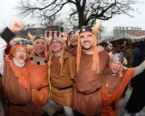 Fröhliche Männer in historischer Wikinger-Kleidung mit Hörnerhelmen und orangefarbenen Perücken feiern ausgelassen.