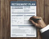 Formularz "RETIREMENT PLAN" do wypełnienia, aby złożyć wniosek o emeryturę. Widoczna ręka z długopisem.
