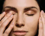Primo piano di una donna con lentiggini, che si tocca il viso. Potrebbe indicare sintomi di carenza vitamina d sulla pelle.