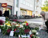 En kvinna lägger blommor vid en minnesplats för Kim Larsen. Många blommor och ljus.