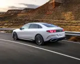 Weißer Mercedes C-Klasse EQ fährt auf einer Straße in bergiger Landschaft.