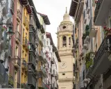 Edificio con balcónes floridos y torre de iglesia en Navarra. ¿Buscas ayudas cambio ventanas Navarra?