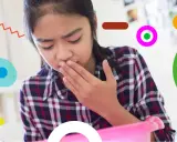 Bambina con nausea, forse per farmaci, copre la bocca con la mano, pronta a vomitare in un contenitore rosa.