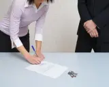 Une femme signe un document, peut-être un passage expert assurance habitation, tandis que des clés reposent sur la table.