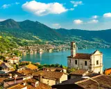 Un borgo pittoresco sul lago, ideale per gite in giornata da Milano. Case con tetti rossi, una chiesa e montagne verdi sullo sfondo.