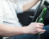 Mężczyzna za kierownicą trzyma butelkę piwa, zastanawiając się, ile promili ma jedno piwo.