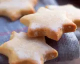 Des sablés au citron en forme d'étoiles, saupoudrés de sucre, reposent sur un tissu bleu.