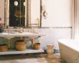 Elegante baño con doble lavabo de mármol, bañera exenta y suelo de baldosas. Un espejo con marco dorado y un cuadro oriental añaden un toque de lujo. ¡Ideas para pintar azulejos baño!