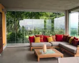 Come arredare una veranda aperta: un divano angolare grigio con cuscini rossi e gialli, un tavolino in legno e una vista sul giardino.