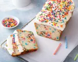 Bunter Konfetti Kuchen mit weißer Glasur und Streuseln. Ein Stück ist angeschnitten und zeigt die bunten Sprenkel im Teig.