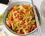 Un plato de chow mein con verduras coloridas y palillos listos para disfrutar.