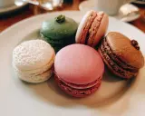 Fem färgglada macarons på en tallrik. En vit med pärlor, en grön, en rosa, en ljusrosa och en brun. Perfekt för ett macarons recept.