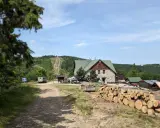 Kamienna chata i stosy drewna przy szlaku na Klimczok. W tle widać górę z wytyczonymi ścieżkami i las.