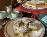 Carrés de croute à thé aux amandes, saupoudrés de sucre glace, servis avec des tasses de thé vert.