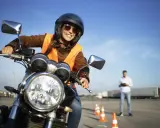 Mujer sonriente con casco y chaleco naranja, lista para obtener su carnet AM B en una autoescuela.