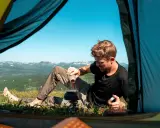 Man förbereder kaffe utanför tältet med en fantastisk utsikt. En del av packlista vandring sommar.