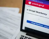 Na ekranie laptopa widoczny jest portal e-Urząd Skarbowy. Obok leżą dokumenty, które mogą zawierać identyfikator zobowiązania.