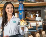 Kelnerka prezentuje deser z menu Schroniska Smaków Bukowina. Wnętrze restauracji zdobią góralskie wzory.