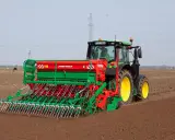 Zielony traktor z siewnikiem Agro-Masz pracuje na polu. Maszyna precyzyjnie wysiewa nasiona, optymalizując ile trawy na hektar zostanie zasiane.