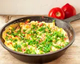 Pyszny omlet z warzywami, posypany szczypiorkiem, gotowy do podania. Obok leżą dwa pomidory.