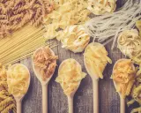 Verschiedene Nudelsorten auf Holzlöffeln und Holzuntergrund. Welche Pasta hat am wenigsten Kalorien? Vielleicht die dünnen Reisnudeln?