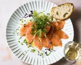 Zarter Saibling, mariniert mit Kräutern und Zitrone, verspricht einen delikaten Geschmack. Dazu ein Stück Brot und ein Glas Weißwein.