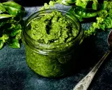 Frisches Basilikum-Pesto in einem Glas, bereit für ein köstliches basilikum pesto rezept. Daneben ein Löffel und grüne Basilikumblätter.