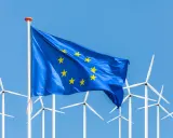 Europäische Flagge weht vor einer Reihe von Windrädern, die für erneuerbare Energien in der EU stehen.