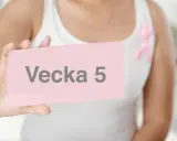 En person håller upp en rosa lapp med texten "Vecka 5". En rosa band pryder personens vita linne.