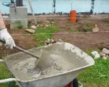 Mano enguantada mezcla cemento y arena en carretilla. Preparando material para construcción.
