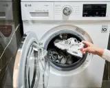 Kobieta wkłada białe buty do pralki, pokazując, jak prać białe buty w pralce.